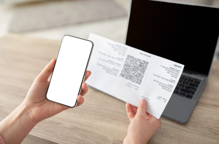 Female hands holding smartphone and scanning the QR code from paper bill, cellphone with white blank screen